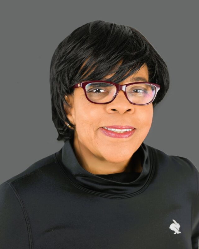Woman wearing glasses and black top against a gray background.