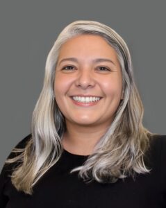 Smiling person with long gray hair against a gray background.