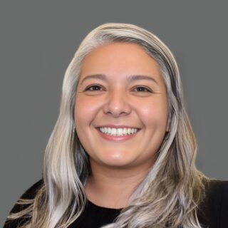 Smiling person with long gray hair against a gray background.
