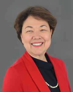 Smiling person in a red blazer with a gray background.