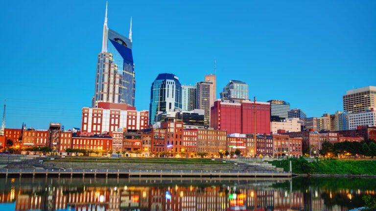 Nashville skyline reflected in the water, featuring modern skyscrapers and historic buildings under a clear blue sky.