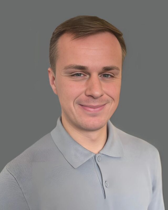 Smiling person in a gray collared shirt against a gray background.