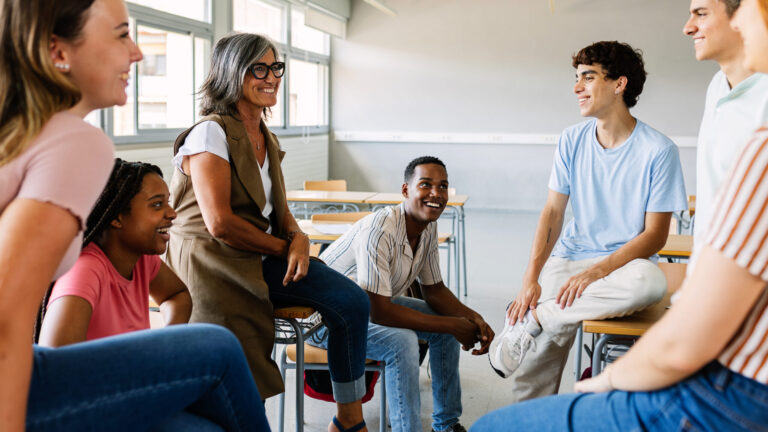 Group of diverse students and teacher sitting and smiling in a classroom setting.