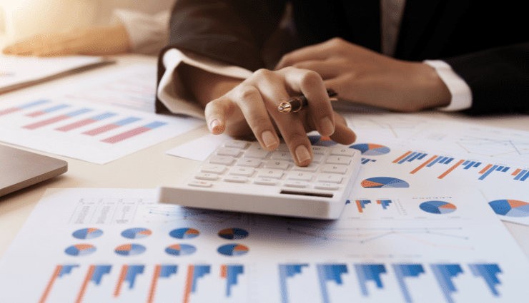 Person using a calculator with financial charts and graphs in the background, analyzing data and statistics.