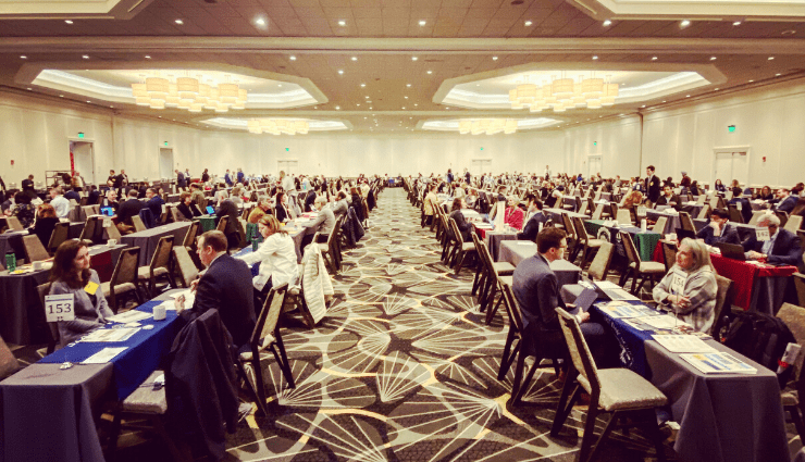 Large conference room filled with seated attendees at a business event, dressed in formal attire.