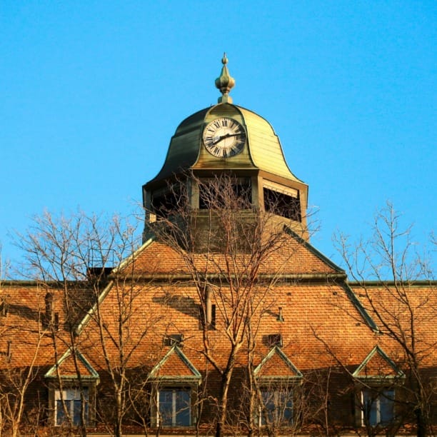 Historic building with a clock tower against a clear blue sky, framed by bare trees in the foreground.