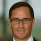 Man with glasses and a suit smiling at the camera.