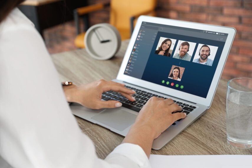 Person typing on a laptop during a video call with four participants visible on the screen.