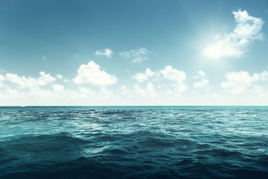 Sunny day with clear blue ocean and fluffy white clouds on the horizon