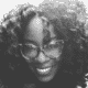 Smiling person with curly hair and glasses in a black and white photo.