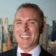 Smiling man in a suit with a city skyline in the background.