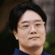 Man wearing glasses, looking at camera, with a blurred background.