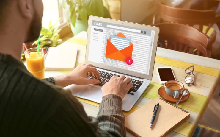 Person typing on a laptop with an email notification on screen, surrounded by a coffee cup and office supplies on a desk.