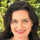 Smiling person with dark hair and earrings in front of leafy green background