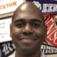 Man smiling in front of a colorful wall with various college pennants.