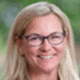 Smiling person with glasses and blonde hair in an outdoor setting.