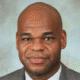 Man in a suit with a neutral expression against a neutral background.