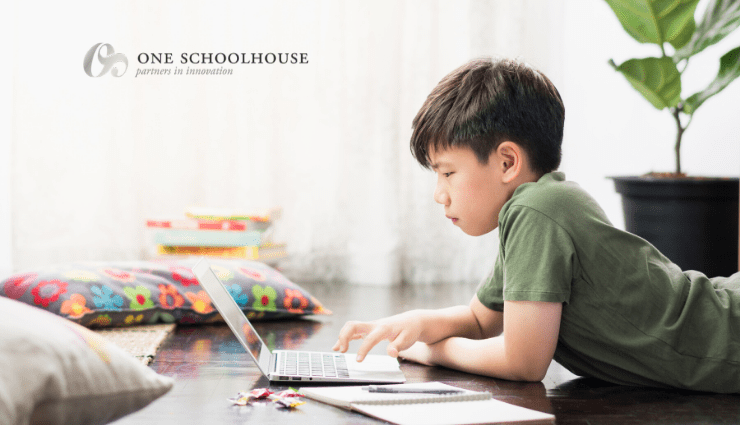 Boy focused on using a laptop at a desk with colorful cushions in a bright room.