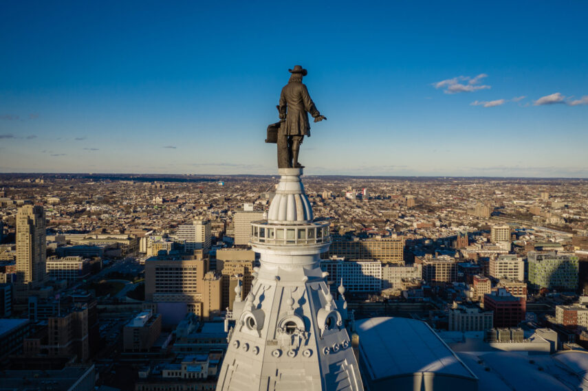 William Penn statue atop Philadelphia City Hall with cityscape in the background under a clear blue sky.