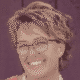 Smiling person with short hair and glasses against a purple background.