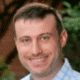 Smiling person outdoors in a checkered shirt with a blurred background.