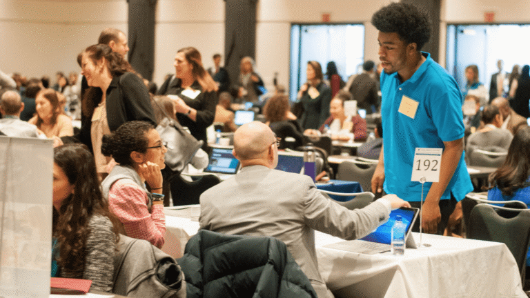 People networking at a busy career fair, with a young person talking to a professional at a table.