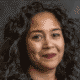 Person with curly hair smiling against a dark background.
