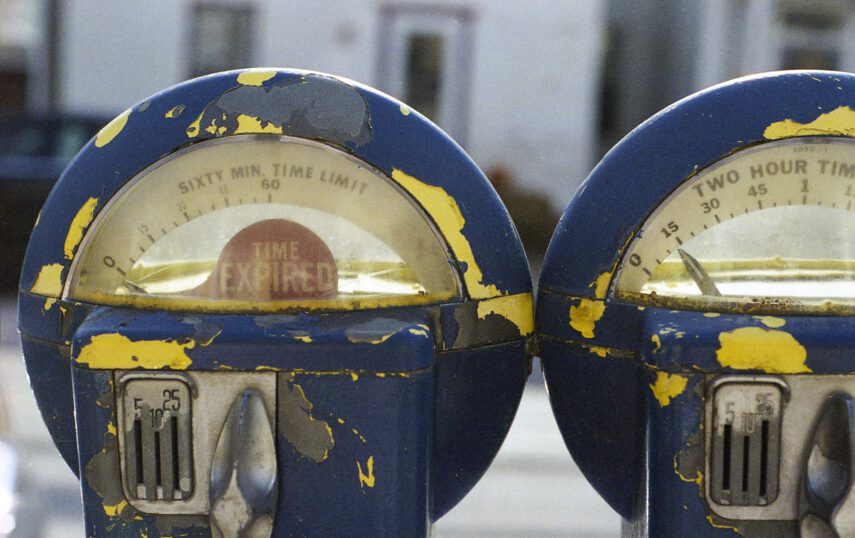 Two old, weathered parking meters with peeling blue paint and visible internal mechanisms, set against a blurry background.