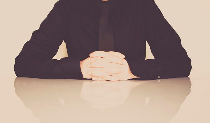 Man in tie sits with folded hands close up