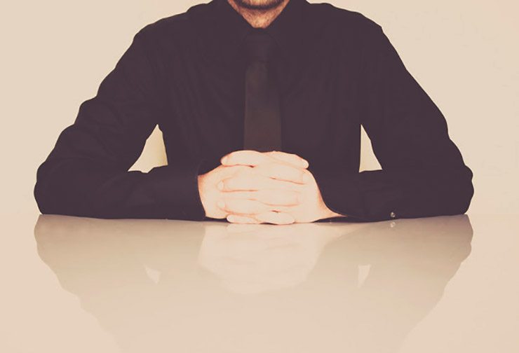 Man in tie sits with folded hands close up
