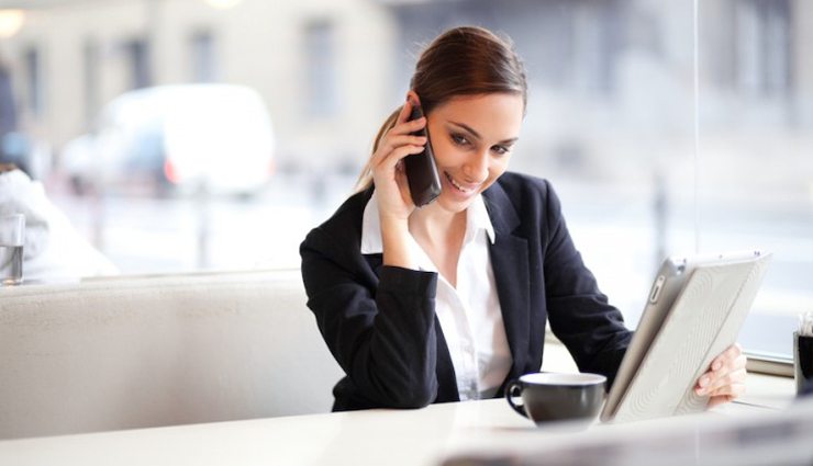 professional woman reads iPad while on the phone with a cup of coffee