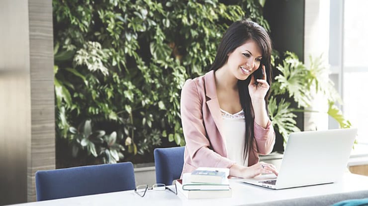 woman works on laptop with books and talks on phone