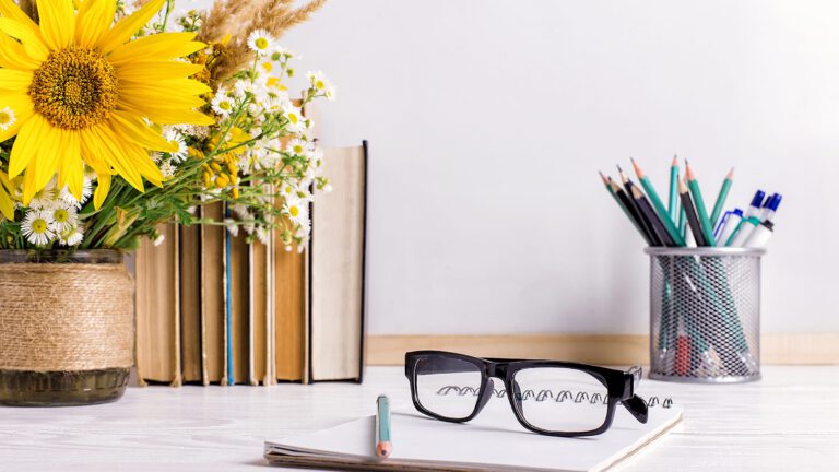 Books, glasses, markers and a bouquet of flowers in a vase on white board background. Concept for teachers day and first September