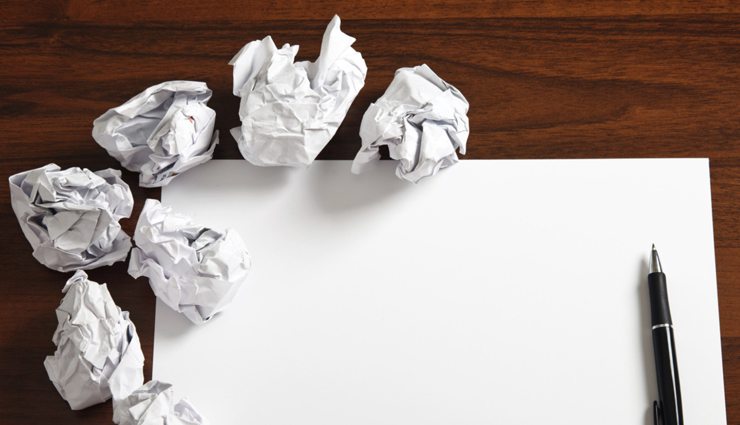 Crumpled pieces of paper on a wooden desk with a blank sheet of paper ready for writing or sketching.