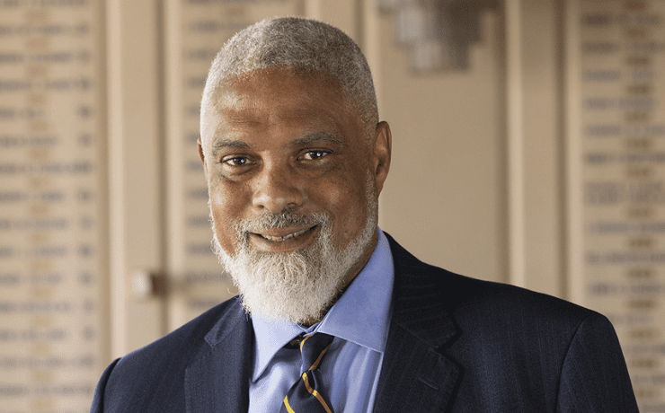 Elderly man with a gray beard and suit smiling in a formal setting.