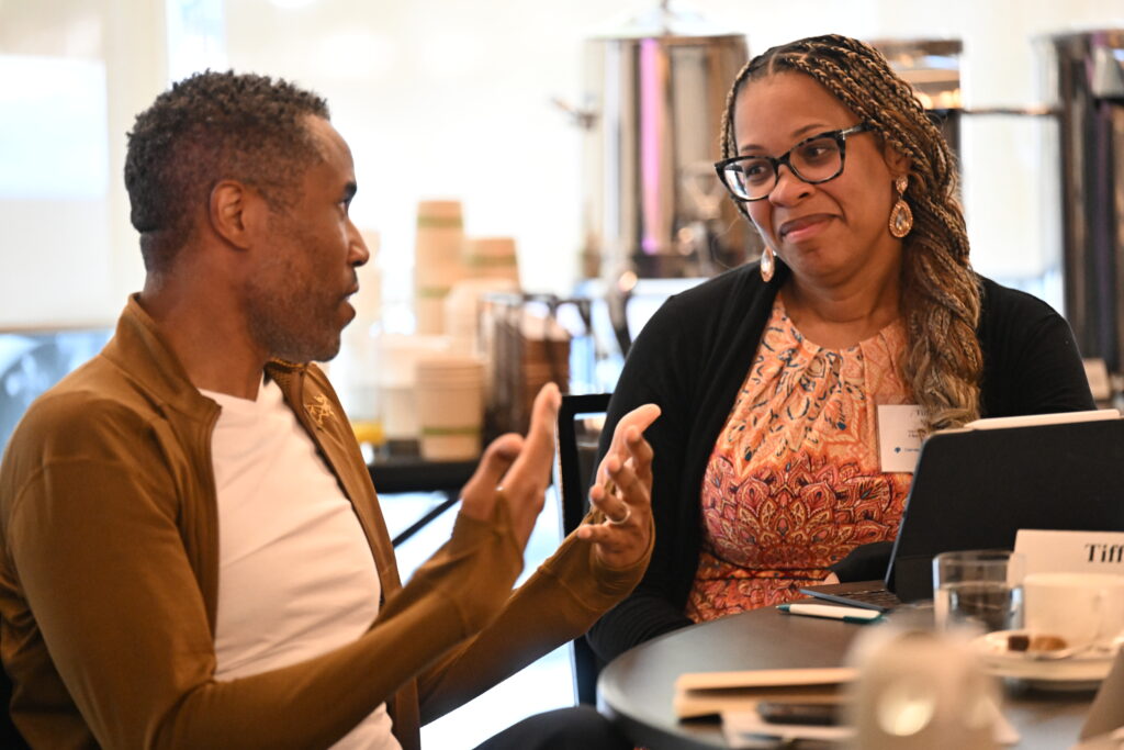 Two people having a conversation at a table, with coffee cups and a warm ambiance in the background.