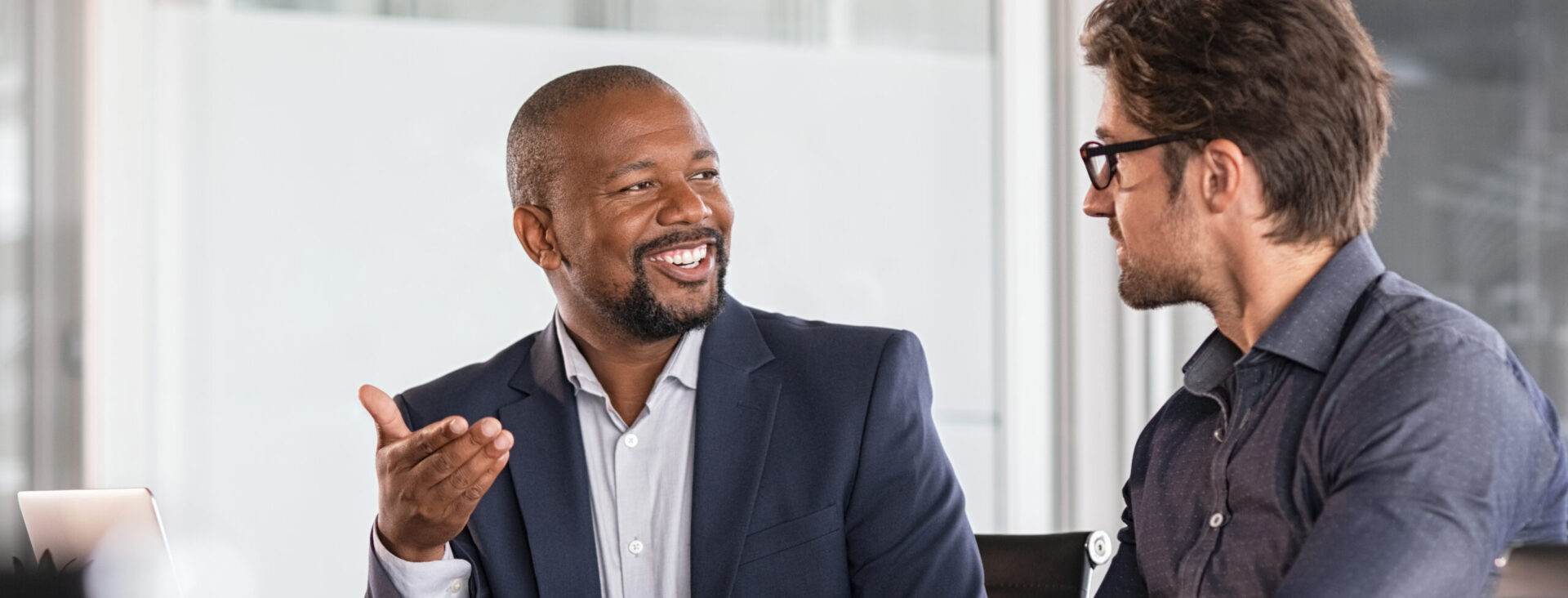 Two businessmen sitting at a table, engaged in a lively discussion in a modern office setting.