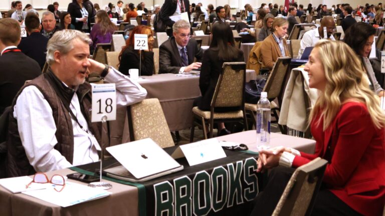 People seated at tables in a conference setting, engaging in discussions and networking activities.