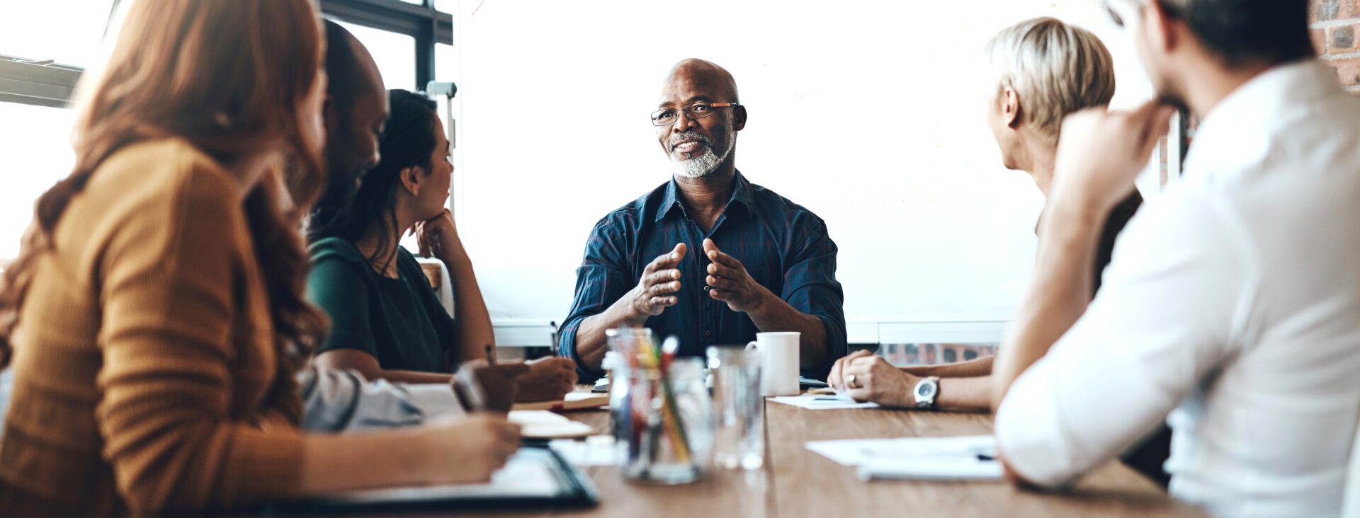 Group of people having a meeting around a wooden table in a modern office setting, discussing and smiling.
