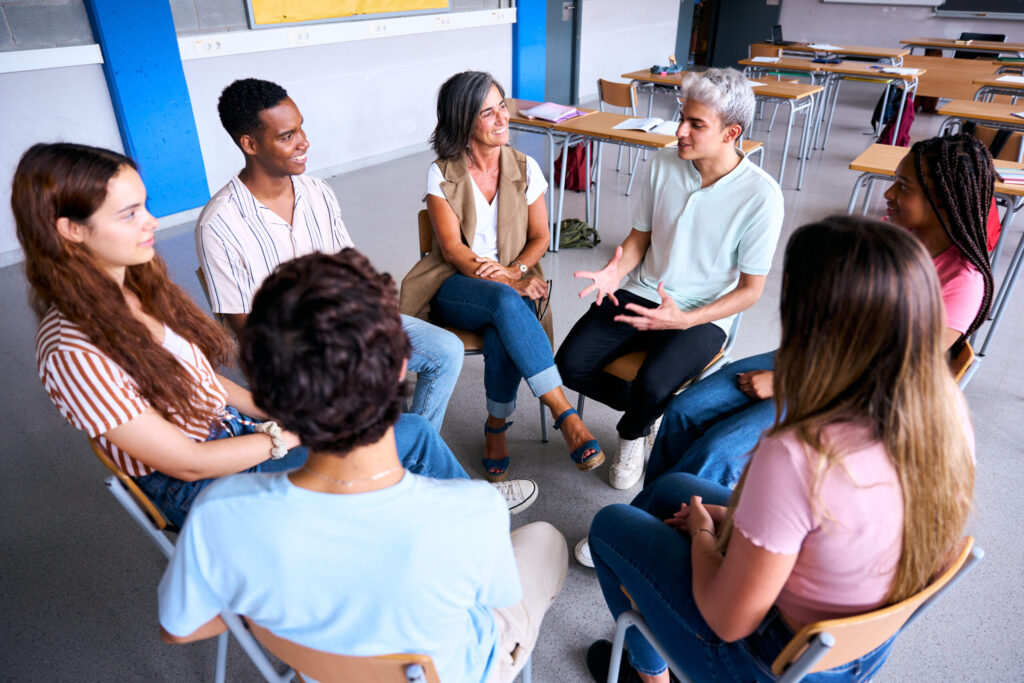 Group of diverse people sitting in a circle having a lively discussion in a bright classroom setting.