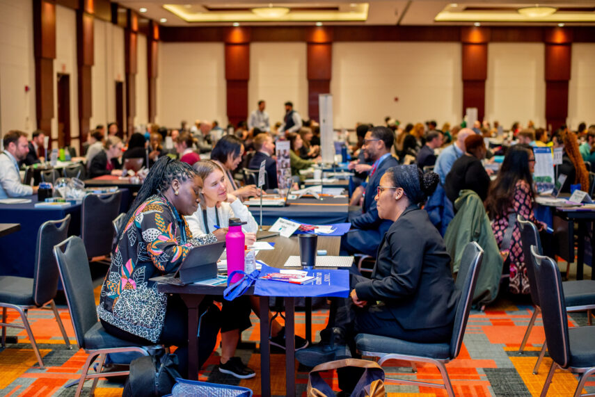 People engaged in conversations at a large networking event, seated at tables in a spacious conference room.