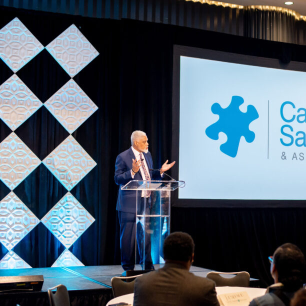 Speaker presenting at Carney Sandoe & Associates event with audience seated and company logo displayed on a screen