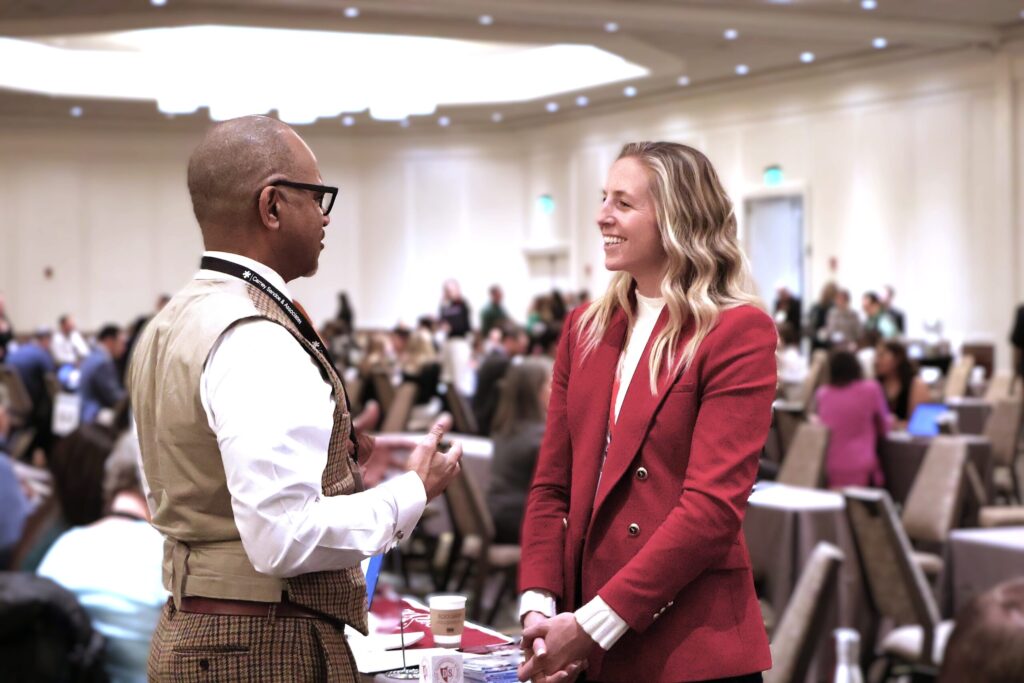 Two people dressed in business attire having a conversation at a professional conference setting.