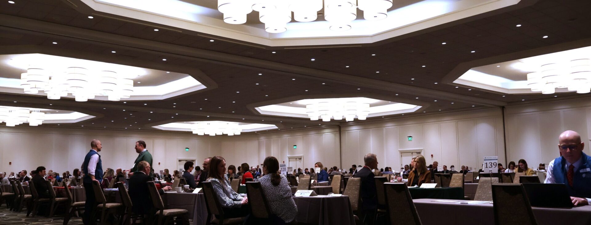 People seated at tables in a large conference room with bright overhead lighting.