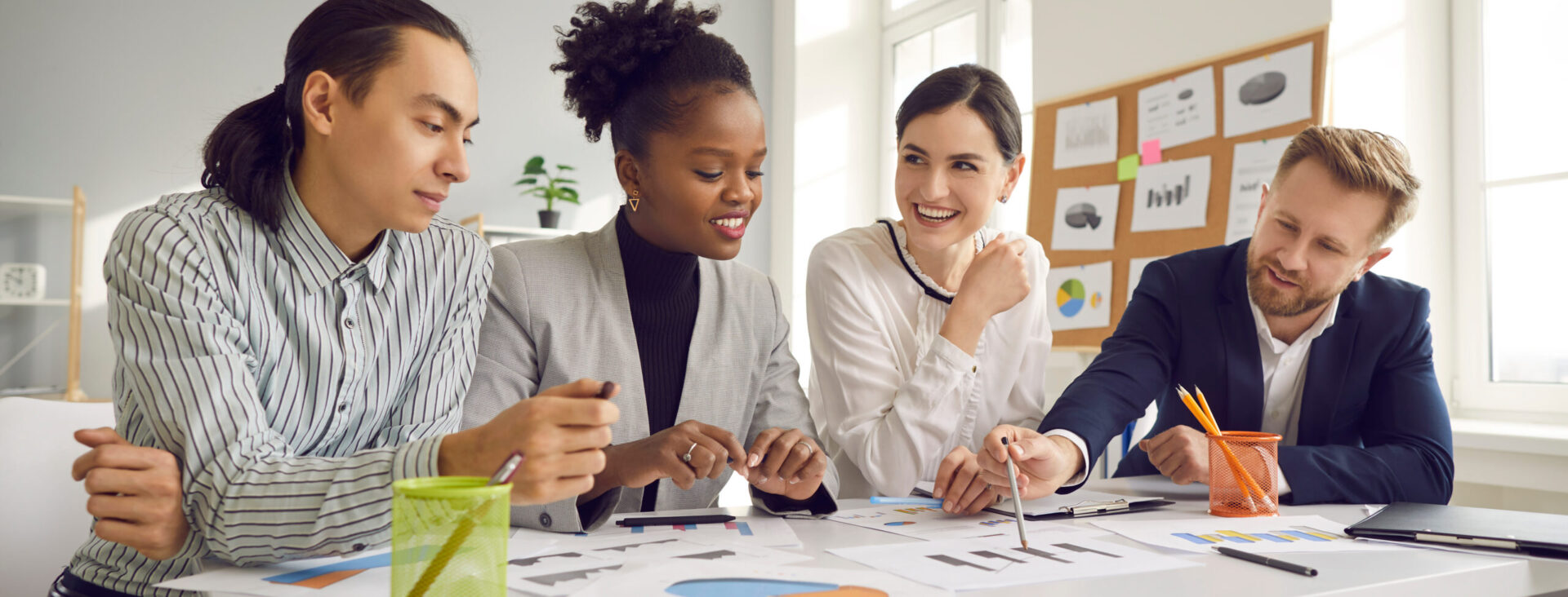 Team collaborating around a table with documents and graphs in a bright office setting.