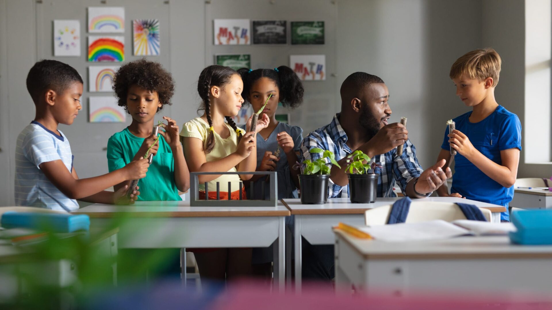 Teacher and diverse children in a classroom engaged in a hands-on plant science activity, colorful artwork on the walls.