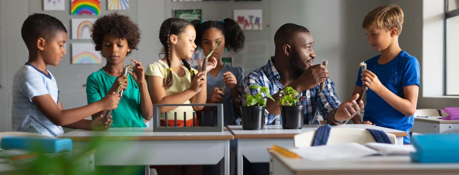 Teacher and diverse children in a classroom engaged in a hands-on plant science activity, colorful artwork on the walls.