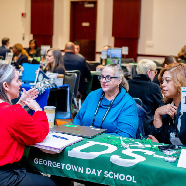 People at a conference table discussing educational materials at a Georgetown Day School booth.