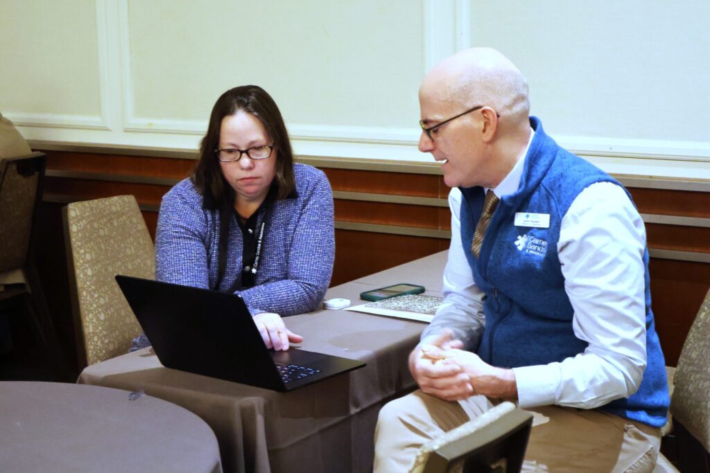 Two people seated at a table looking at a laptop screen during a discussion in a conference room.