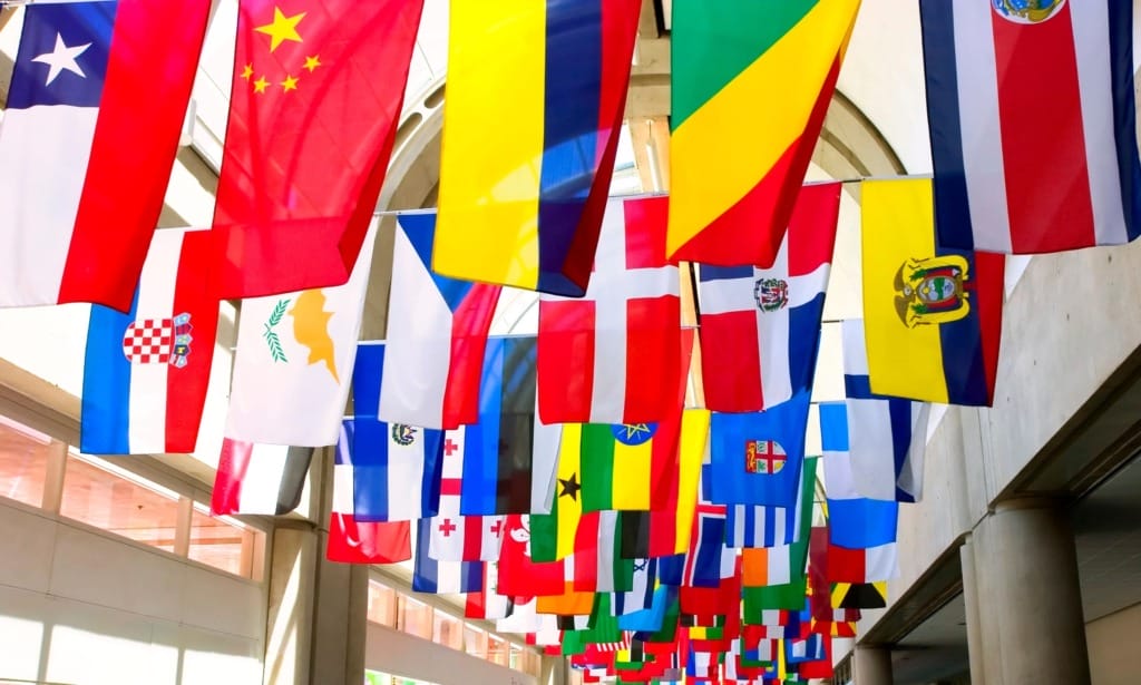 Colorful international flags hanging from a high ceiling in an indoor space with natural light filtering through windows